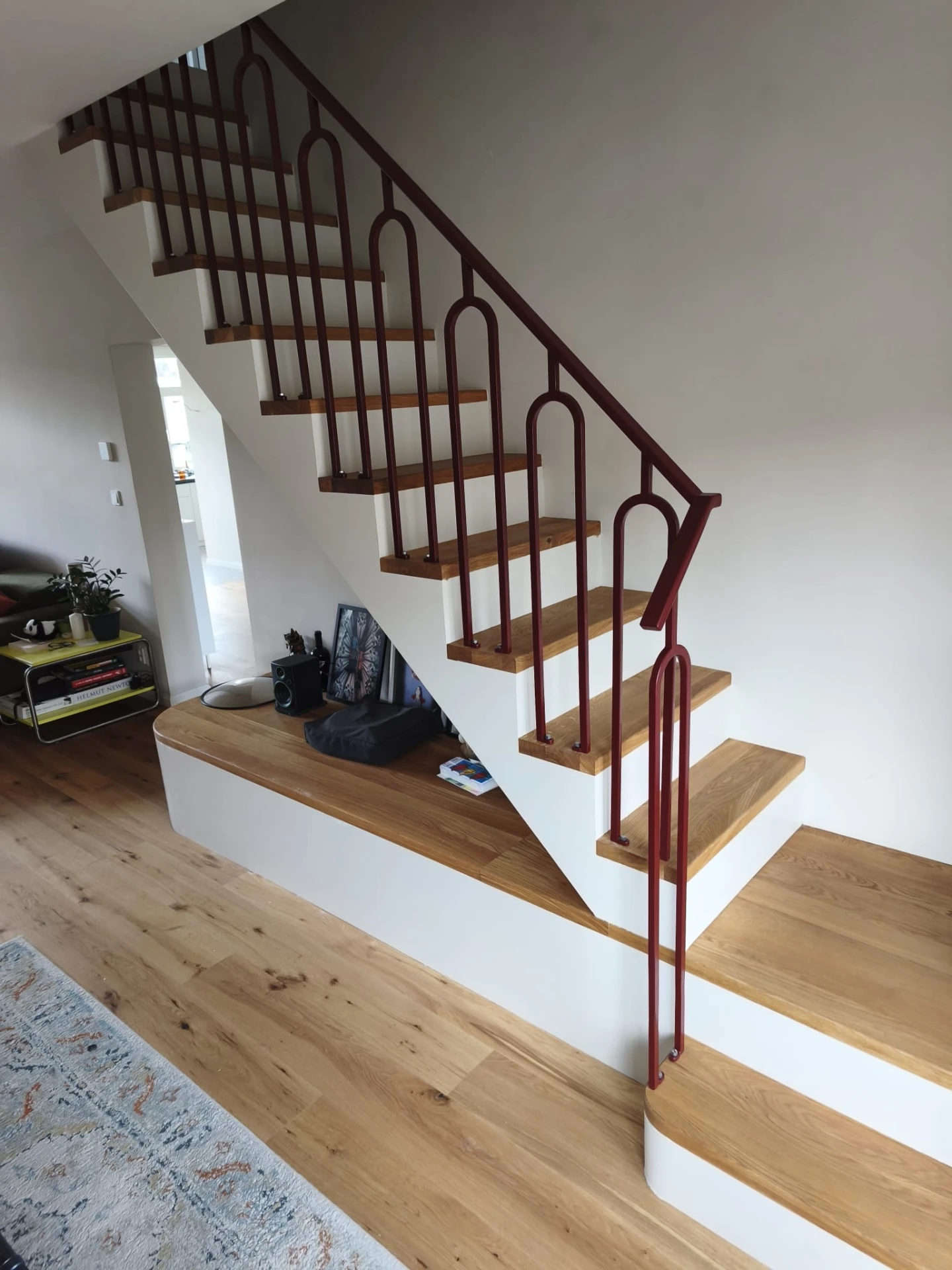 Maatwerk stalen balustrade in wijnrood (RAL 3005 mat) met afgeronde langwerpige vormen langs een houten trap in Amsterdam-West, gemaakt door Kevco